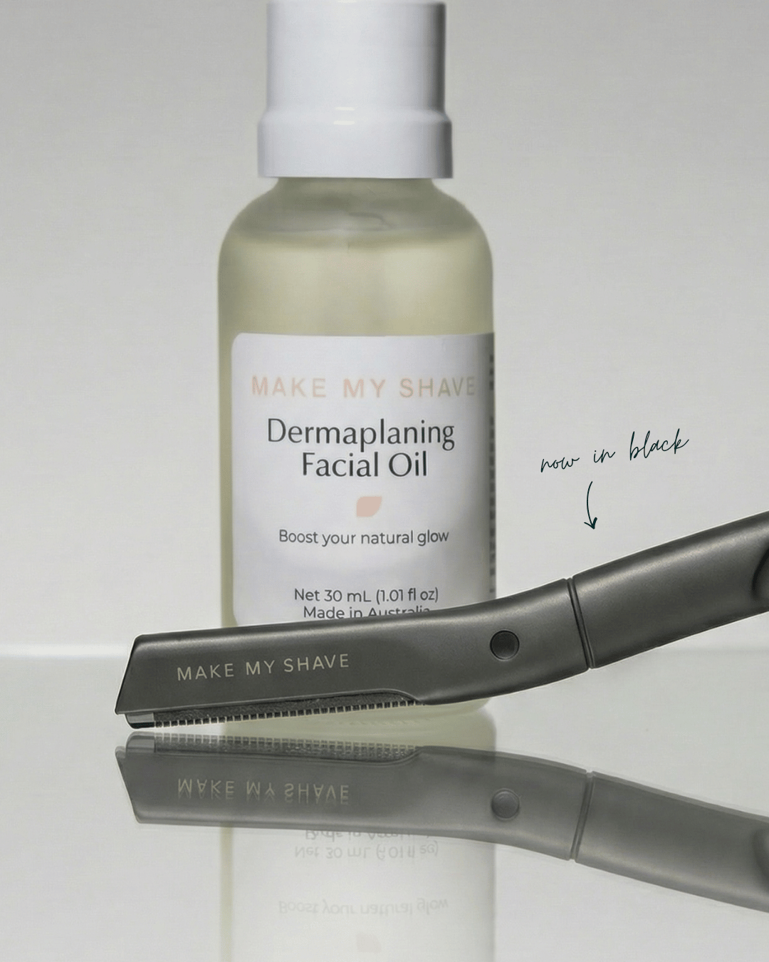 Bottle of 'Make My Shave' dermaplaning facial oil with a black dermaplaning kit on a reflective surface.