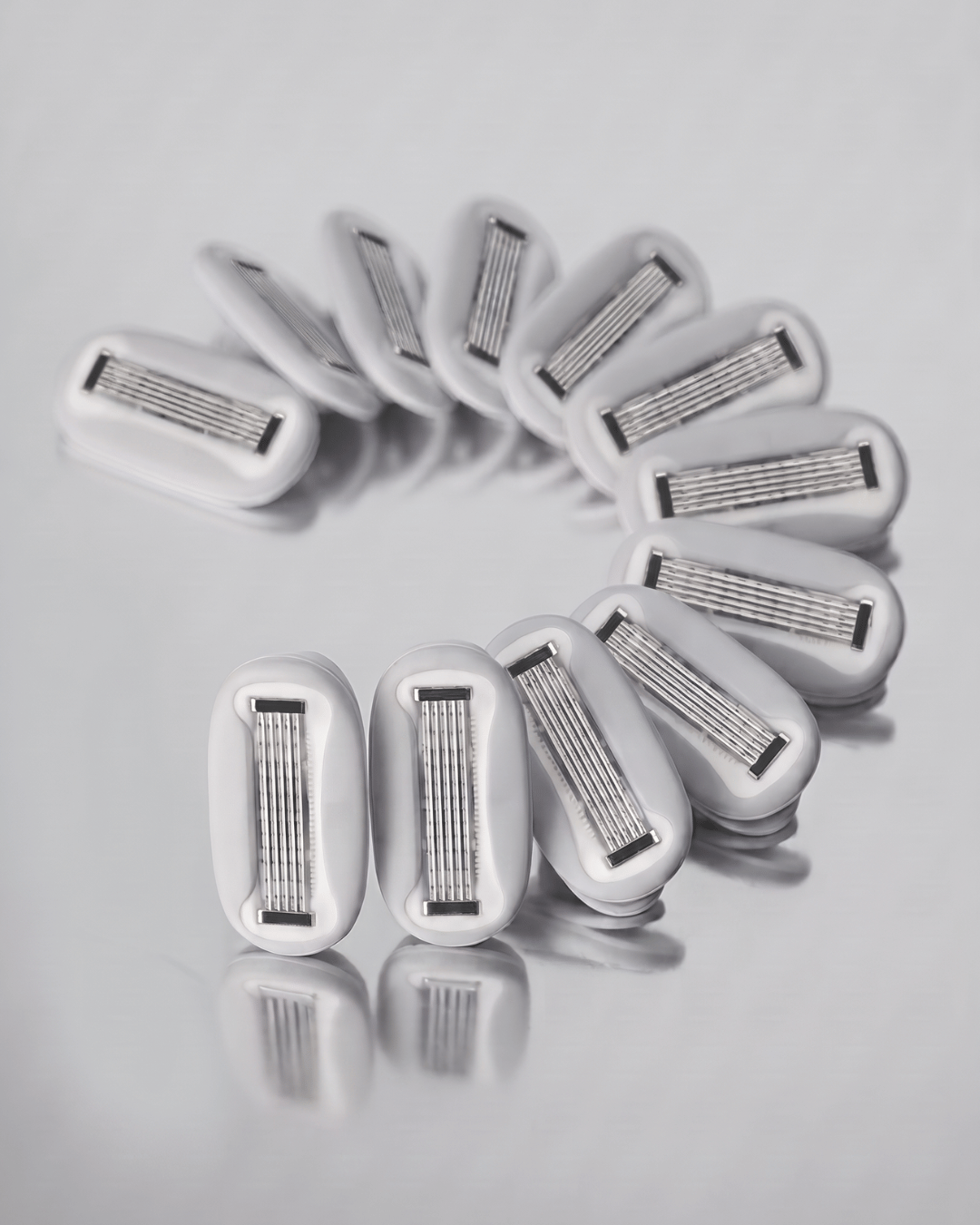 Twelve women's razor cartridge 5-blade razor heads arranged in a loose circle on a light grey reflective surface.
