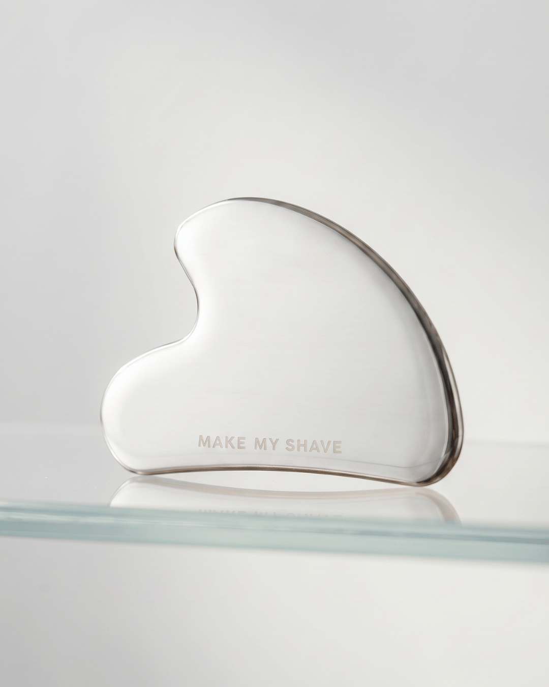 Steel Gua Sha on glass shelf, by Make My Shave