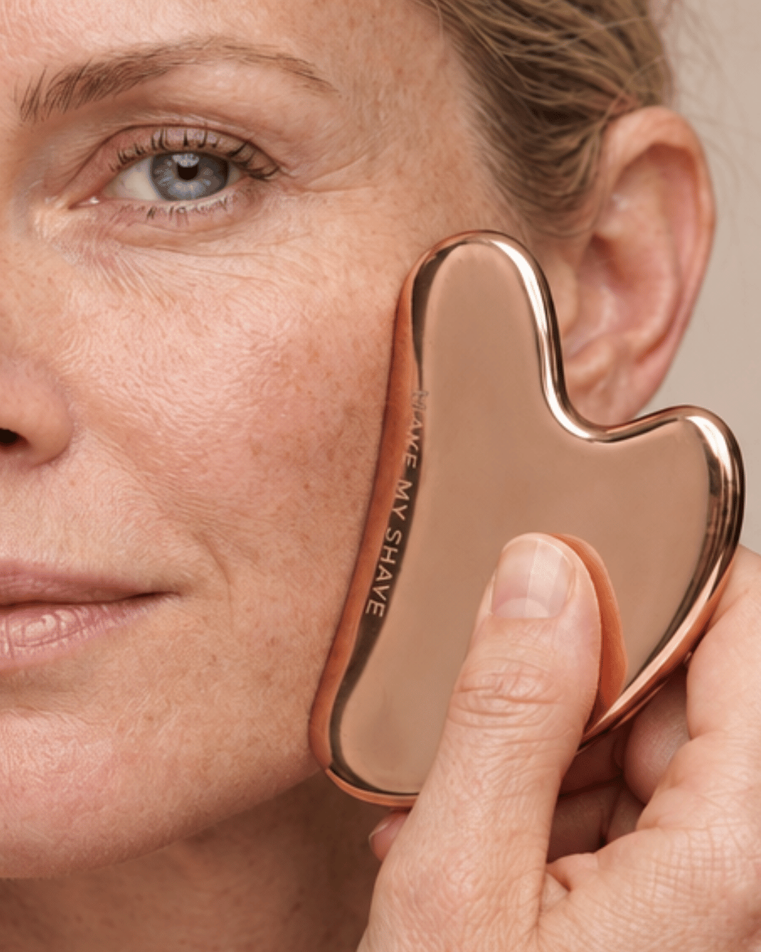 Rose Gold Gua Sha by Make My Shave, Australia being used to smooth a woman's jawline and cheek.