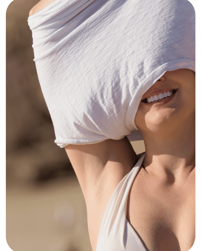 Woman with a white cloth over her head, smiling outdoors. Her armpits are smooth from using her Make My Shave women's razor