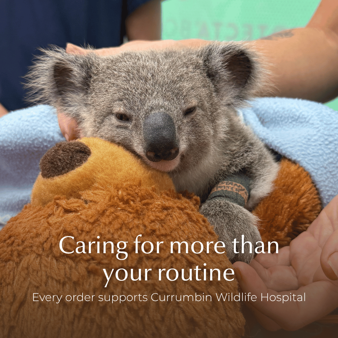 A koala recovering holding a brown plush toy, with overlaid text reading 'Caring for more than your routine' and 'Every order supports Currumbin Wildlife Hospital', sustainable shave care by Make My Shave.